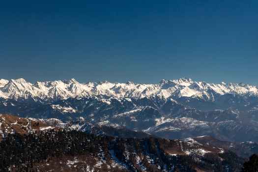 View of snow capped mountains under a crisp blue sky create a stunning winter landscape with dark green trees dotting the lower slopes Lasdana Azad Kashmir Pakistan.