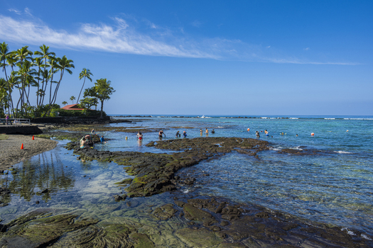 Aerial view of Kahalu u Beach Park with turquoise waters volcanic rock formations and people snorkeling under a clear blue sky Kailua Kona Hawaii United States. Aerial view of Kahalu u Beach Park with turquoise waters volcanic rock formations and people snorkeling under a clear blue sky Kailua Kona Hawaii United States.