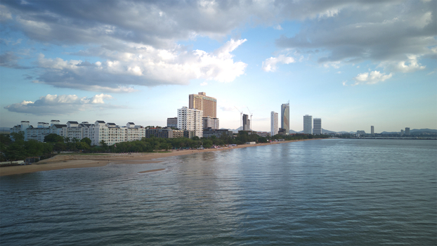 Aerial view of Jomtien Beach featuring high rise hotels along the sandy coastline under a dramatic cloudy sky in Chon Buri Thailand.