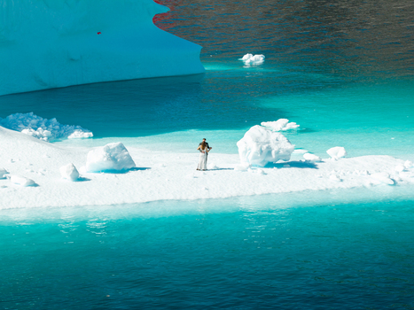 Aerial view of a couple standing on a small iceberg surrounded by turquoise glacial water and larger ice formations in Greenland. Aerial view of a couple standing on a small iceberg surrounded by turquoise glacial water and larger ice formations in Greenland.