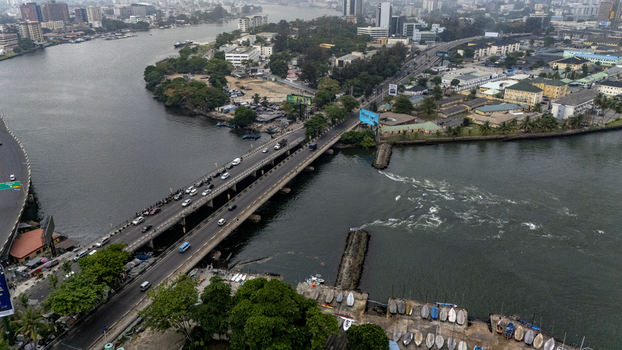 Aerial view of the bridge connecting to Lagos Island featuring heavy traffic surrounding urban buildings and boats moored along the waterfront in Lagos Lagos Nigeria. Aerial view of the bridge connecting to Lagos Island featuring heavy traffic surrounding urban buildings and boats moored along the waterfront in Lagos Lagos Nigeria.