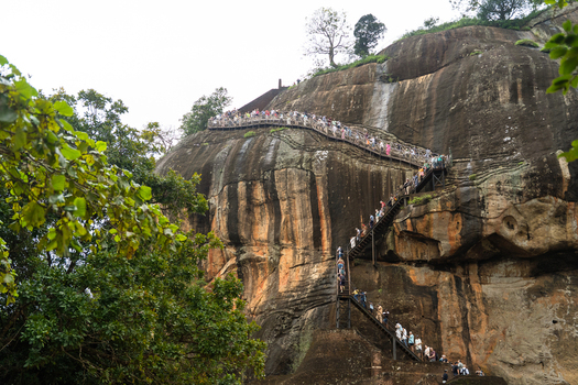 Sri Lanka 21 February 2026 View of tourists climbing the steep metal staircase on the side of the ancient Sigiriya rock fortress with weathered rock face and lush tropical greenery.