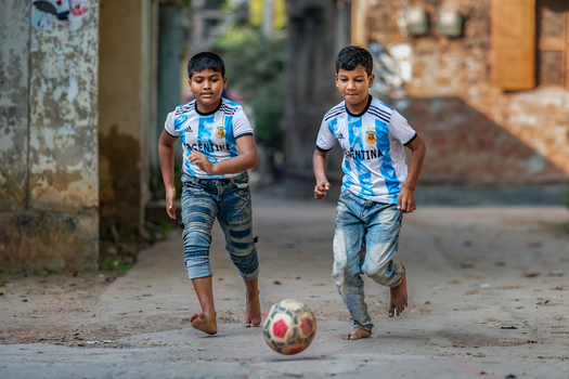 Bogura Rajshahi Division Bangladesh 30 November 2022 View of two young boys wearing Argentina national football team jerseys playing soccer barefoot on a dusty street.