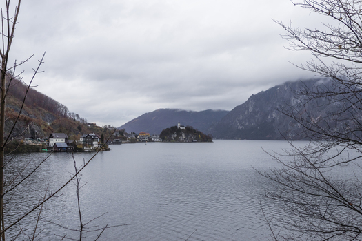 View of the calm waters of Hallstatter See surrounded by steep mountains and traditional alpine houses under an overcast sky in Hallstatt Upper Austria Austria. View of the calm waters of Hallstatter See surrounded by steep mountains and traditional alpine houses under an overcast sky in Hallstatt Upper Austria Austria.