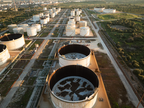 Aerial view of a large industrial oil storage facility with cylindrical tanks and complex pipeline networks under warm afternoon light in Augusta Sicily Italy. Aerial view of a large industrial oil storage facility with cylindrical tanks and complex pipeline networks under warm afternoon light in Augusta Sicily Italy.