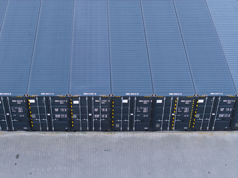 Aerial view of rows of blue shipping containers arranged in a neat line on a paved industrial yard in Poland. Aerial view of rows of blue shipping containers arranged in a neat line on a paved industrial yard in Poland.