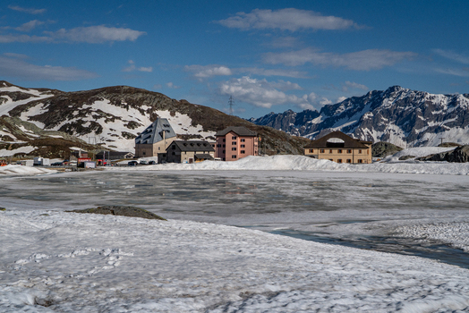 View of the Sankt Gotthard Pass featuring a frozen lake and historic buildings surrounded by snow capped mountains in Airolo Ticino Switzerland.
