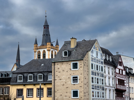 View of the historic St. Gangolf church tower rising above traditional timber framed buildings and stone facades under a cloudy sky in Trier Rheinland Pfalz Germany.