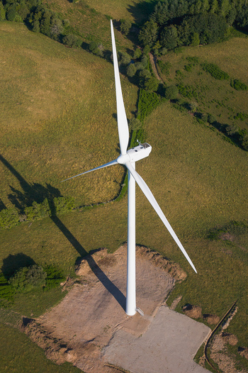 Aerial view of a stark white wind turbine standing tall against the patchwork of green and brown fields casting a long shadow Salles Curan Occitanie France. Aerial view of a stark white wind turbine standing tall against the patchwork of green and brown fields casting a long shadow Salles Curan Occitanie France.