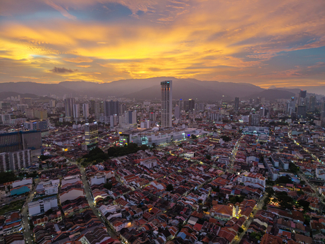 George Town Malaysia 22 September 2026 Aerial view of George Town cityscape at sunset with historic rooftops modern skyscrapers and distant mountains under a golden sky.