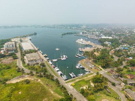 Aerial view of the harbor with yachts and catamarans docked at piers surrounded by palm trees and industrial buildings in Galle Southern Province Sri Lanka.