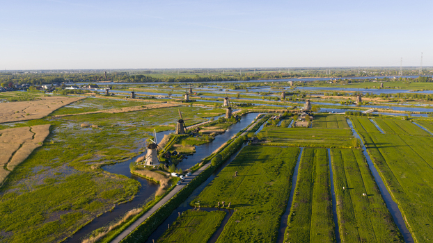 Aerial view of historic windmills standing along narrow canals amidst lush green fields and polder landscapes under a clear blue sky Kinderdijk South Holland Netherlands. Aerial view of historic windmills standing along narrow canals amidst lush green fields and polder landscapes under a clear blue sky Kinderdijk South Holland Netherlands.