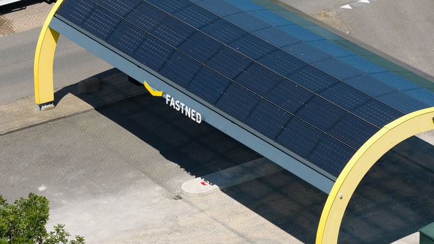 Middenbeemster Netherlands 20 June 2026 Aerial view of Fastned Charging Station featuring a distinctive yellow arched roof covered with solar panels in a paved parking area.