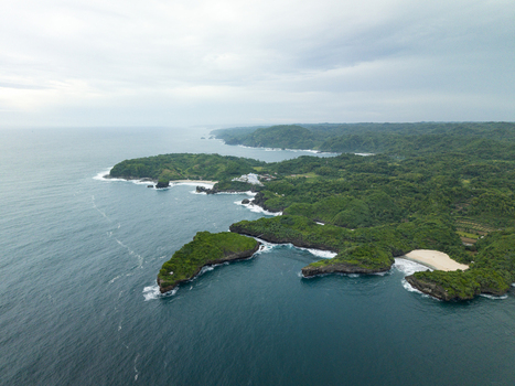Aerial view of Sedahan Beach where the turquoise waters meet the lush green headlands and rocky outcrops under a vast sky Gunungkidul Regency Special Region of Yogyakarta Indonesia. Aerial view of Sedahan Beach where the turquoise waters meet the lush green headlands and rocky outcrops under a vast sky Gunungkidul Regency Special Region of Yogyakarta Indonesia.