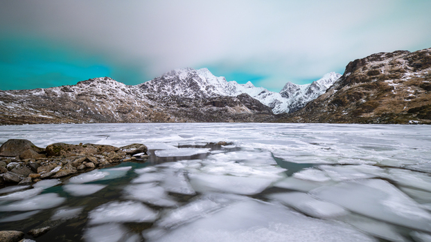 View of a frozen lake with ice floes and snow capped mountains under an overcast sky in Leknes Lofoten Norway.