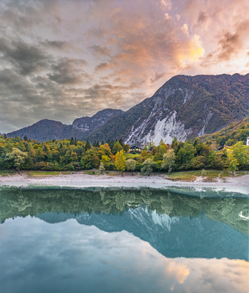 Aerial view of Lago di Tenno with turquoise waters reflecting the surrounding autumn forest and mountain peaks under a vibrant sunset sky in Tenno Trentino Alto Adige Italy.