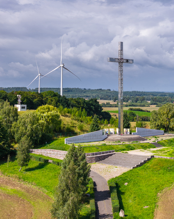 Aerial view of John Paul II Hill and Memorial with a large metal cross green hills wind turbines and a pathway leading to the monument in Pelplin Pomeranian Voivodeship Poland. Aerial view of John Paul II Hill and Memorial with a large metal cross green hills wind turbines and a pathway leading to the monument in Pelplin Pomeranian Voivodeship Poland.