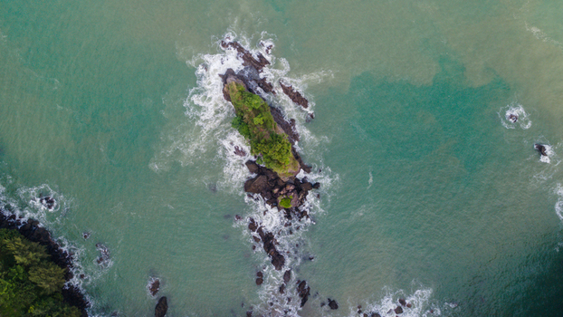 Aerial view of the rocky islet of Karang Agung surrounded by turquoise sea water and crashing waves with white foam Ayah Central Java Indonesia. Aerial view of the rocky islet of Karang Agung surrounded by turquoise sea water and crashing waves with white foam Ayah Central Java Indonesia.