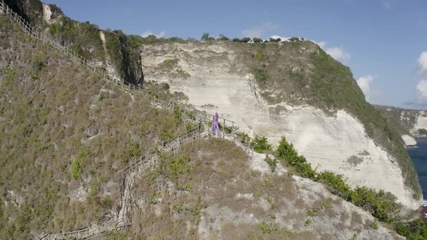 Aerial view of a woman on a steep cliff staircase in Nusa Penida Indonesia. Aerial view of a woman on a steep cliff staircase in Nusa Penida Indonesia.