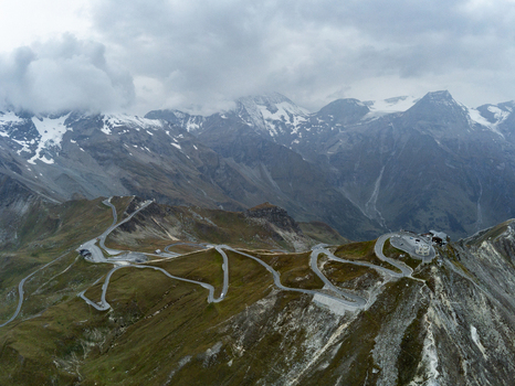 Aerial view of the Grossglockner High Alpine Road winding through the rugged mountain landscape with snow capped peaks and cloudy skies in Zell am See District Salzburg Austria.