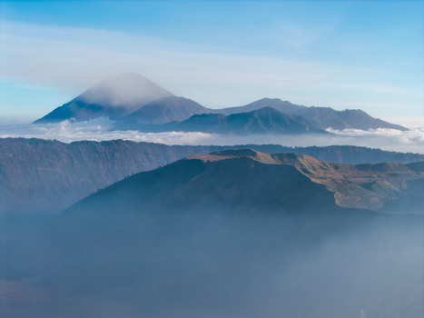 Aerial view of Mount Bromo with Mount Semeru in the background featuring volcanic craters rugged ridges and a sea of clouds under a clear sky in Tosari East Java Indonesia.