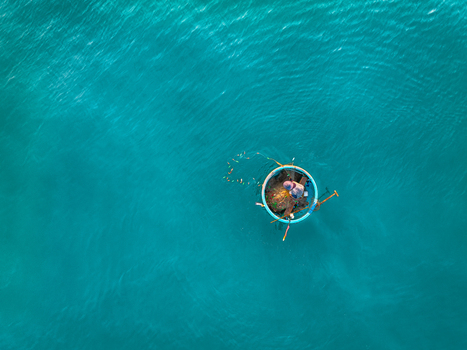 Aerial view of a fisherman in a traditional round basket boat floating on clear turquoise sea water in Vietnam. Aerial view of a fisherman in a traditional round basket boat floating on clear turquoise sea water in Vietnam.