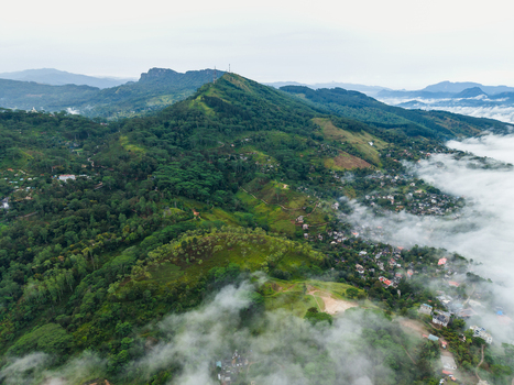 Aerial view of lush green mountains and a village partially covered by thick white mist in Kandy Central Province Sri Lanka. Aerial view of lush green mountains and a village partially covered by thick white mist in Kandy Central Province Sri Lanka.