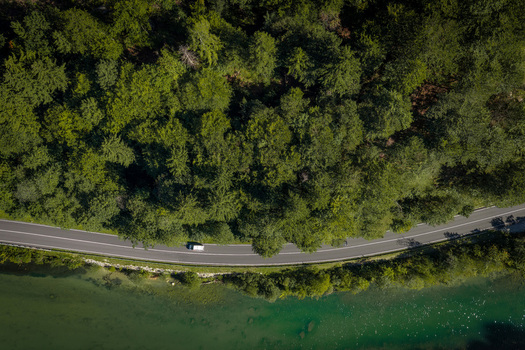 Aerial view of a road winding along the Sava Bohinjka river through a dense forest in Radovljica Slovenia.