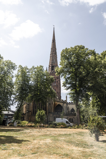 View of the historic stone spire of St Michael s Church rising above lush green trees in Coventry England United Kingdom.