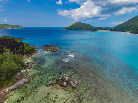 Aerial view of the coastline where turquoise waters meet lush greenery with distant islands under a bright sky Port Launay Mahe Island Seychelles. Aerial view of the coastline where turquoise waters meet lush greenery with distant islands under a bright sky Port Launay Mahe Island Seychelles.