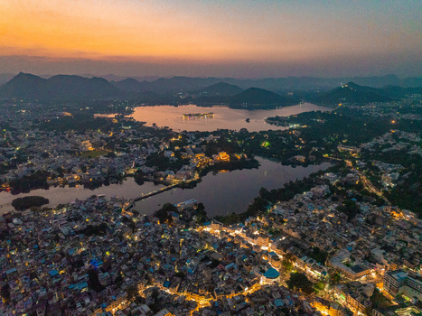 Aerial view of the illuminated city of Udaipur and Lake Pichola at twilight featuring the historic Jag Mandir island palace surrounded by hills in Udaipur Rajasthan India.