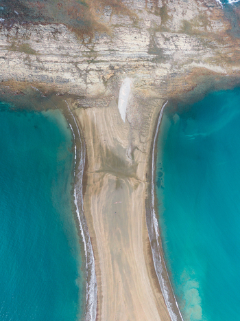 Aerial view of a sandy tombolo connecting to a rocky coastline surrounded by turquoise ocean water in Costa Rica.