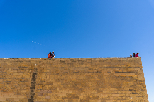 View of people sitting on top of a high limestone fortification wall under a clear blue sky in Zebbug Gozo Region Malta. View of people sitting on top of a high limestone fortification wall under a clear blue sky in Zebbug Gozo Region Malta.
