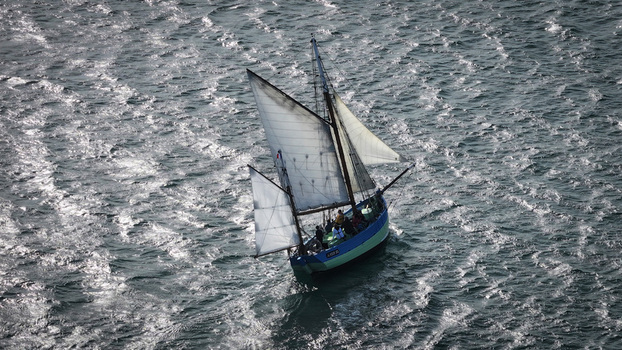 Aerial view of a sailboat slicing through the choppy sun drenched waves of the sea its white sails contrasting against the dark blue hull Plouezoc h Bretagne France. Aerial view of a sailboat slicing through the choppy sun drenched waves of the sea its white sails contrasting against the dark blue hull Plouezoc h Bretagne France.