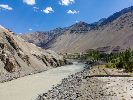 Aerial view of the Indus River flowing through the rugged mountainous landscape of Ladakh with rocky slopes lush green trees along the riverbank and a clear blue sky in Ladakh Ladakh India. Aerial view of the Indus River flowing through the rugged mountainous landscape of Ladakh with rocky slopes lush green trees along the riverbank and a clear blue sky in Ladakh Ladakh India.