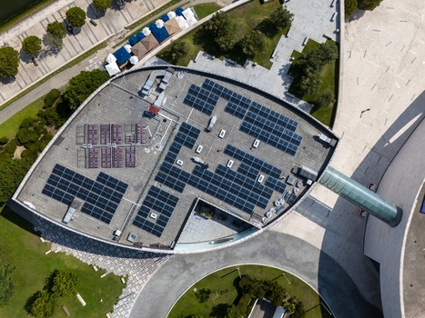Aerial view of solar panels installed on a modern building roof surrounded by paved walkways and green landscaping in Lisboa Lisboa Portugal.