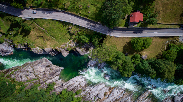 Aerial view of the turquoise Verzasca river flowing through rocky banks next to a winding mountain road and a house with a red roof in Valle Verzasca Verzasca Ticino Switzerland. Aerial view of the turquoise Verzasca river flowing through rocky banks next to a winding mountain road and a house with a red roof in Valle Verzasca Verzasca Ticino Switzerland.