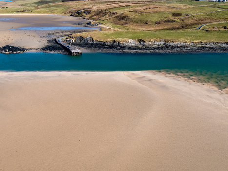 Aerial view of Ballyness Bay with its expansive sandy beach turquoise water and a small stone pier extending into the bay surrounded by green coastal hills in Ballyness County Donegal Ireland. Aerial view of Ballyness Bay with its expansive sandy beach turquoise water and a small stone pier extending into the bay surrounded by green coastal hills in Ballyness County Donegal Ireland.