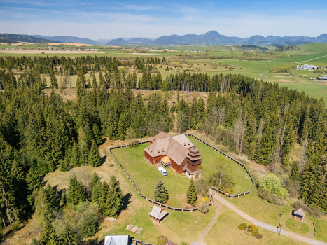 Aerial view of the Wooden Articular Church of Svaty Kriz surrounded by lush evergreen forests and rolling hills under a clear blue sky in Svaty Kriz Zilinsky kraj Slovakia.