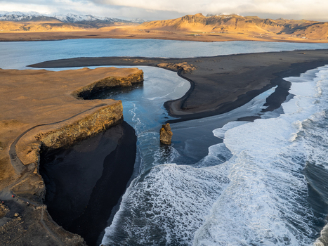 Aerial view of Dyrholaey featuring dramatic black sand beaches rugged cliffs and crashing ocean waves under golden hour light in Myrdalshreppur Iceland. Aerial view of Dyrholaey featuring dramatic black sand beaches rugged cliffs and crashing ocean waves under golden hour light in Myrdalshreppur Iceland.