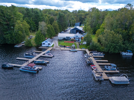 Aerial view of Baptiste Lake marina with numerous boats docked at wooden piers surrounded by lush green forest in Hastings Highlands Ontario Canada.
