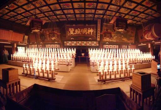 View of the interior of Hakusan Shrine illuminated by rows of glowing candles featuring traditional wooden architecture and ornate ceiling details in Niigata Niigata Japan.