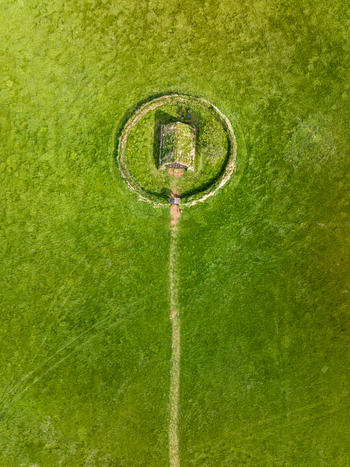 Aerial view of a historic turf roofed church enclosed within a circular stone wall in a vast green field in Iceland. Aerial view of a historic turf roofed church enclosed within a circular stone wall in a vast green field in Iceland.