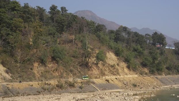 View of a green bus driving on a mountain road by a river Nepal.