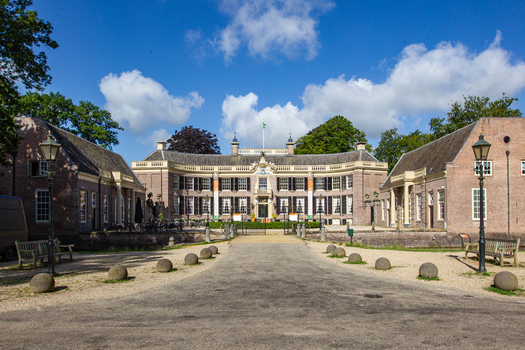 View of Castle Groeneveld historic estate with its grand brick facade side wings and gravel driveway under a blue sky with white clouds in Baarn Utrecht Netherlands.