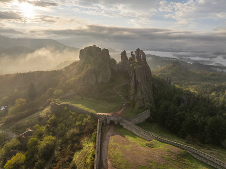 Aerial view of Belogradchik Fortress surrounded by dramatic rock formations lush green hills and morning mist under a soft sunrise in Belogradchik Vidin Bulgaria. Aerial view of Belogradchik Fortress surrounded by dramatic rock formations lush green hills and morning mist under a soft sunrise in Belogradchik Vidin Bulgaria.