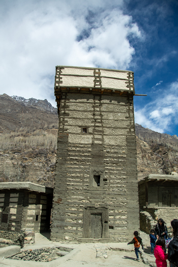 View of the historic Altit Fort with its traditional stone and timber architecture set against rugged mountains with people in the foreground in Altit Gilgit Pakistan. View of the historic Altit Fort with its traditional stone and timber architecture set against rugged mountains with people in the foreground in Altit Gilgit Pakistan.