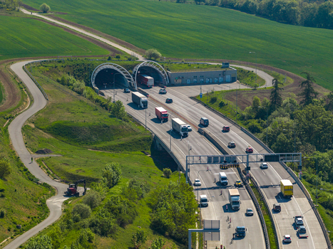 Aerial view of a highway tunnel entrance with heavy traffic including trucks and cars surrounded by green fields and rolling hills in Prague Prague Czechia.