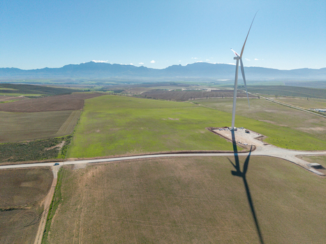 Aerial view of a large wind turbine standing in green agricultural fields with mountains in the background Swellendam Western Cape South Africa. Aerial view of a large wind turbine standing in green agricultural fields with mountains in the background Swellendam Western Cape South Africa.
