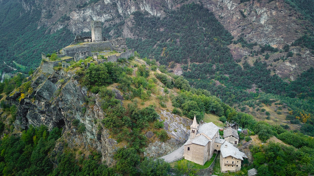 Aerial view of the medieval Saint Germain Castle ruins and the church on a rocky cliff surrounded by lush green forests in Montjovet Aosta Valley Italy.